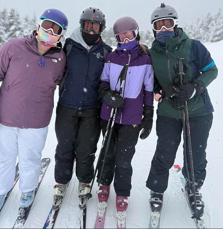 Three ski students and ski club advisor pose for a picture in their ski gear, helmets with flurries of snow. 