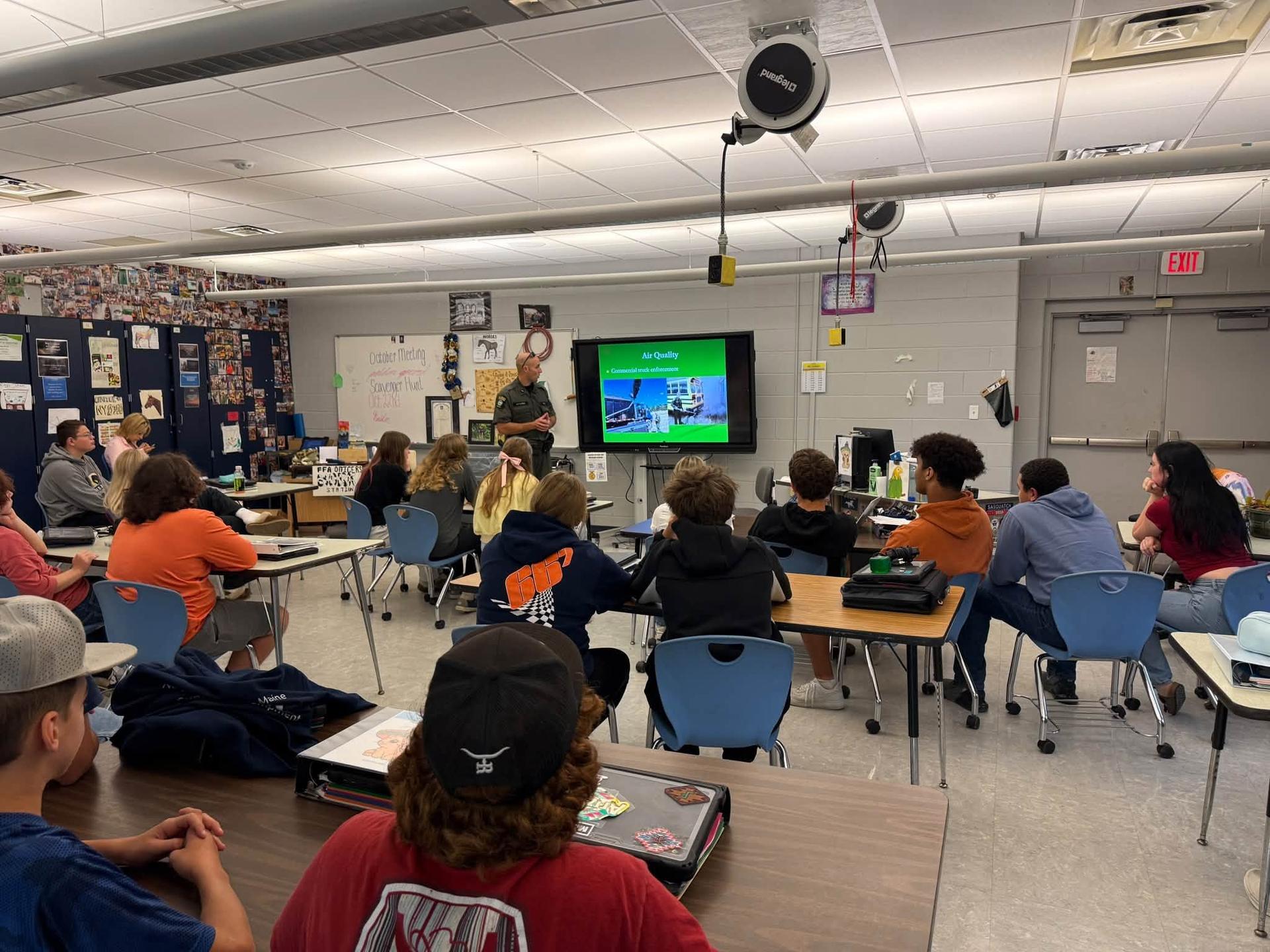 A group of students face an EnCon Officer as he presents. 