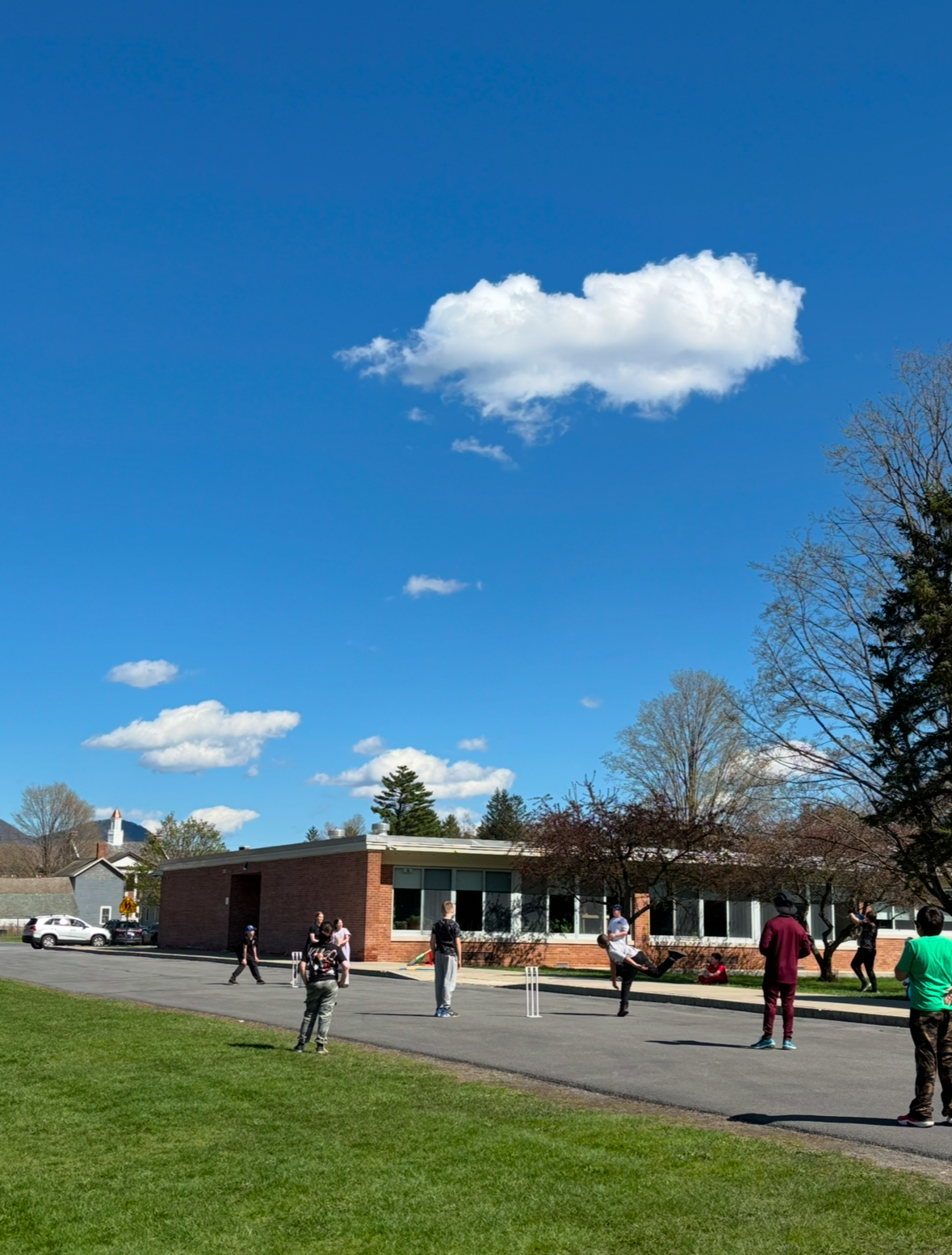 A group of GES students, boys and girls, at GES, playing Cricket with Mr. Rochlani on the side of the GES building. 