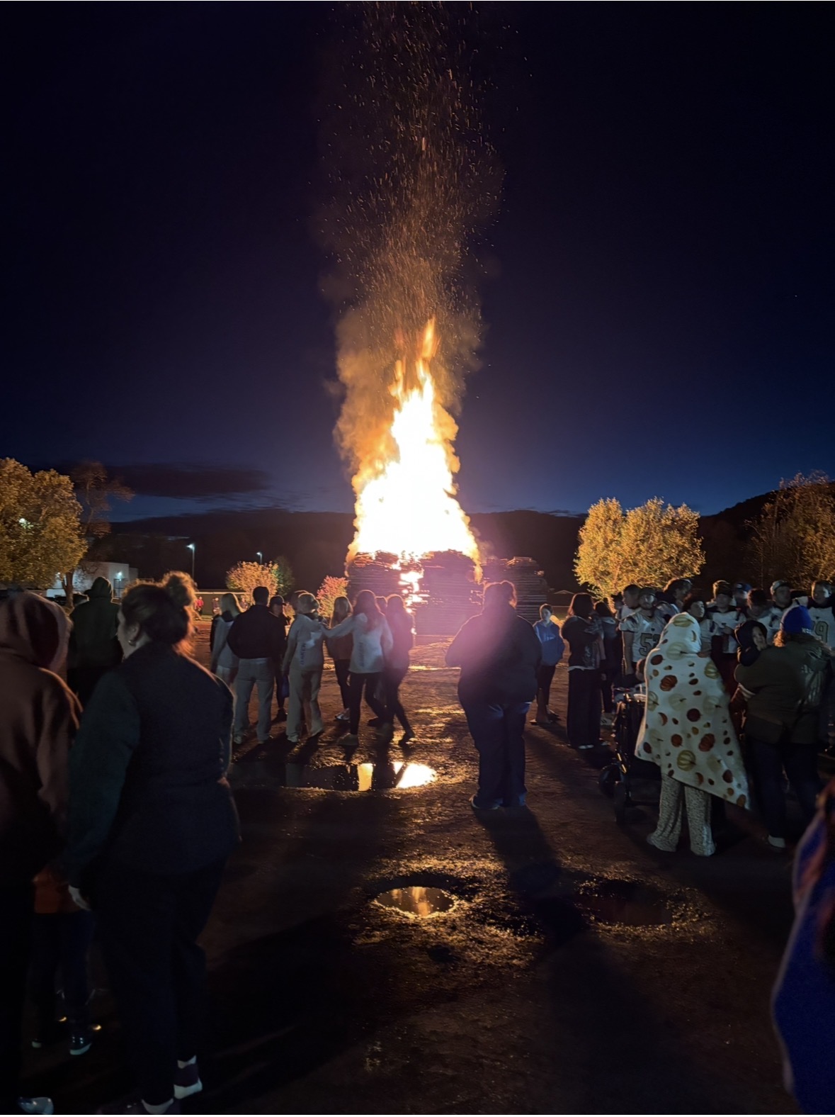 A picture of the a large bonfire with the back of students and families facing the fire