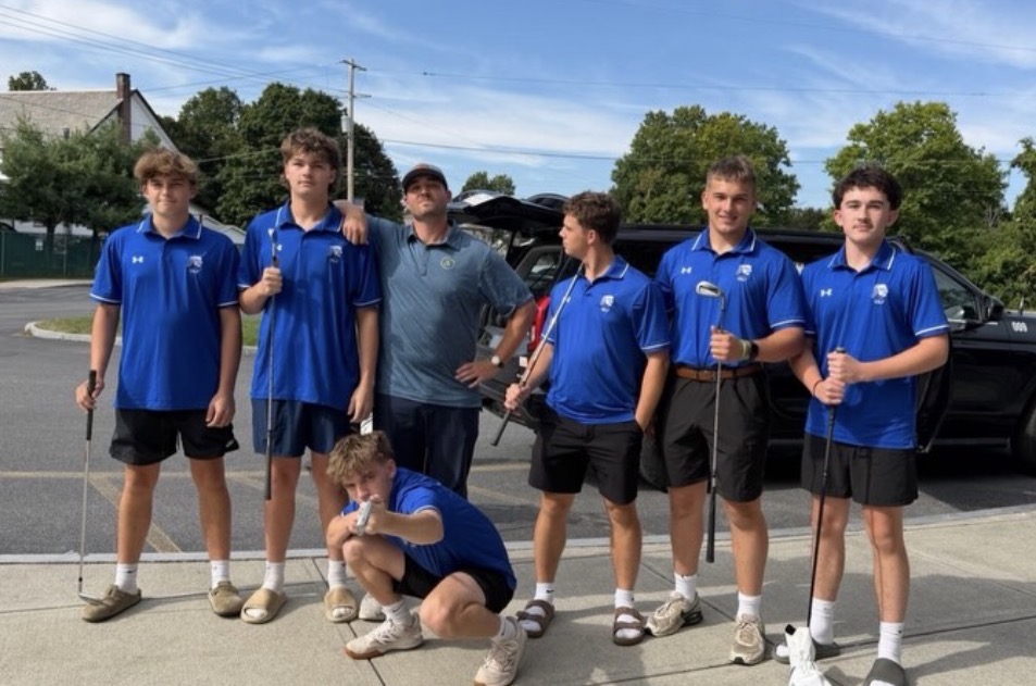 The varsity golf team and their coach stand together, some in funny poses. 