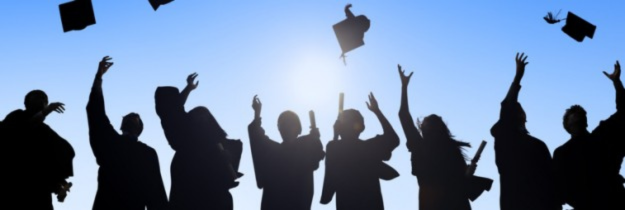 Silhouettes of graduates throwing caps against a blue sky