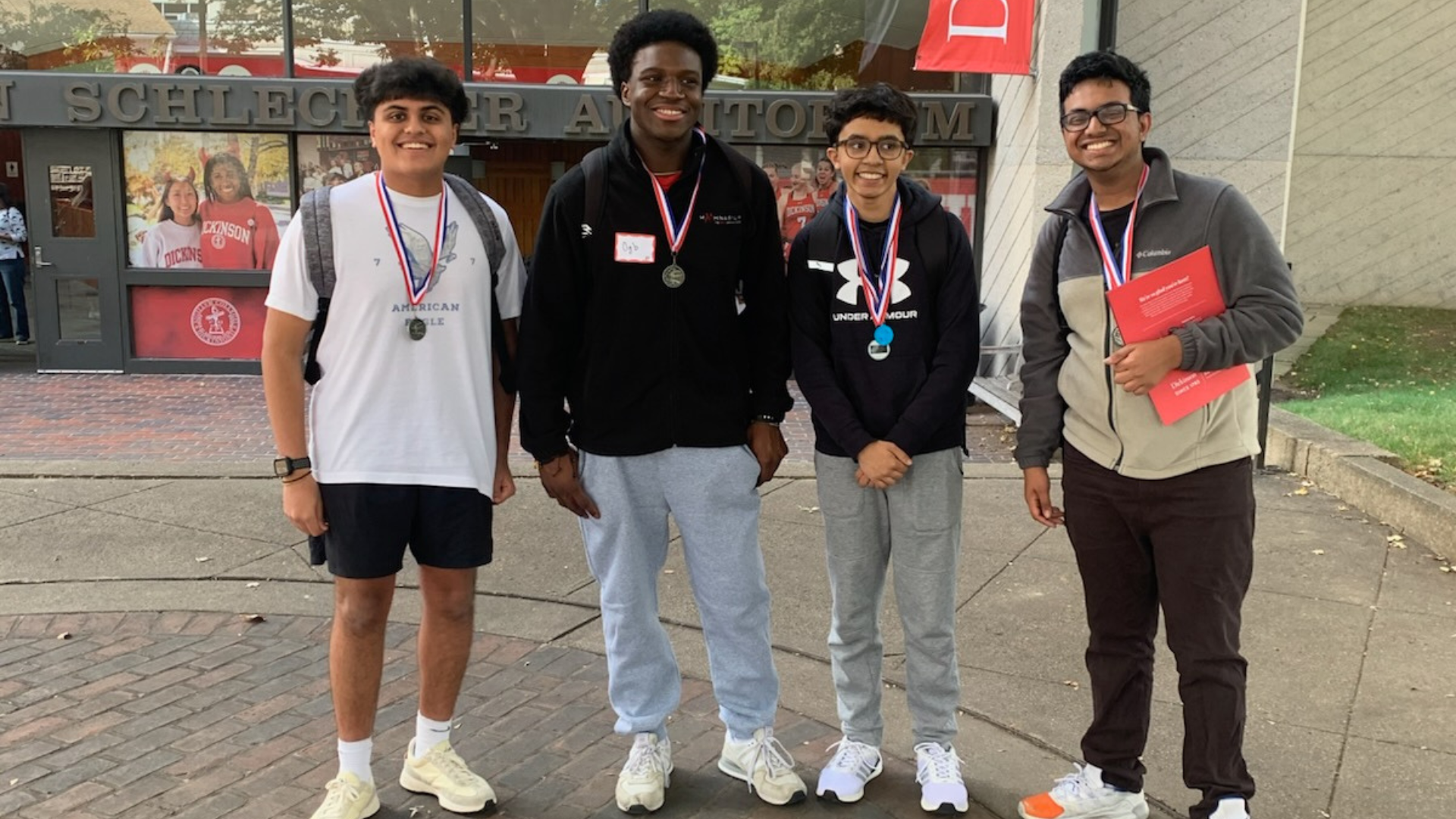 CV math team standing outside Schlechter Auditorium at Dickinson College, wearing medals and holding a red folder after placing second in the Carlisle Interscholastic Math Competition.