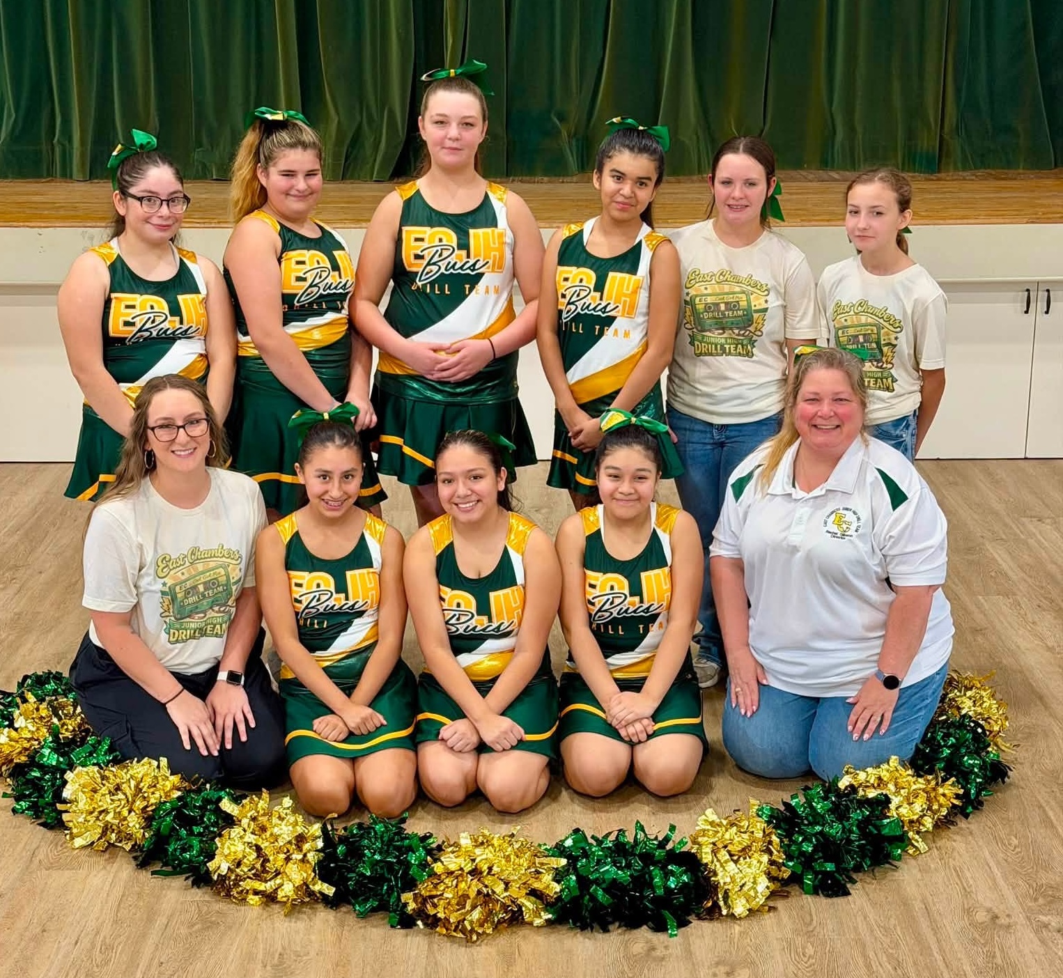 nine drill team members and two coaches in the middle of a gym with poms on the floor