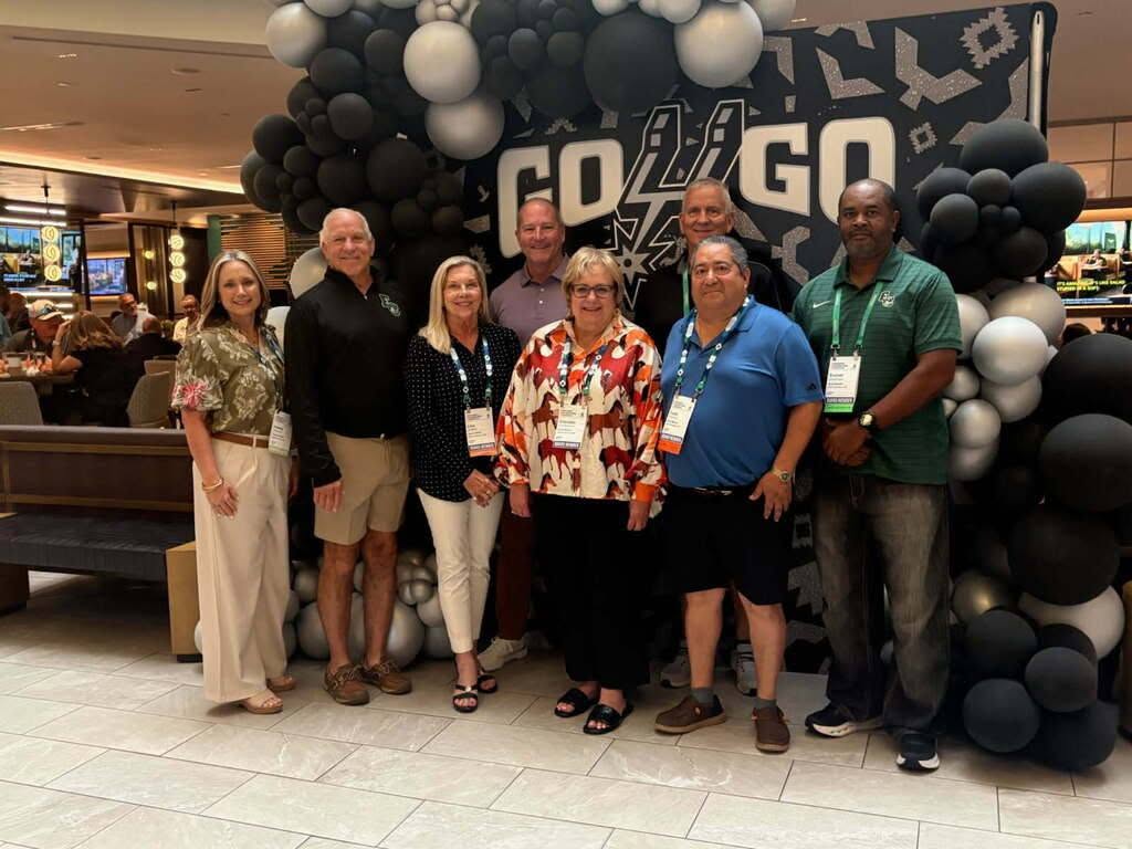 seven board of trustee members with superintendent in front of balloon photo backdrop
