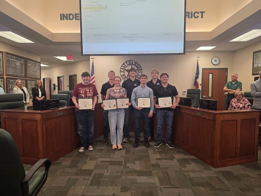 seven students pose with framed certificates in front of board table