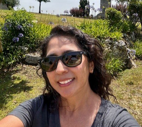 self photo of woman in sunglasses with green grass and trees in the background