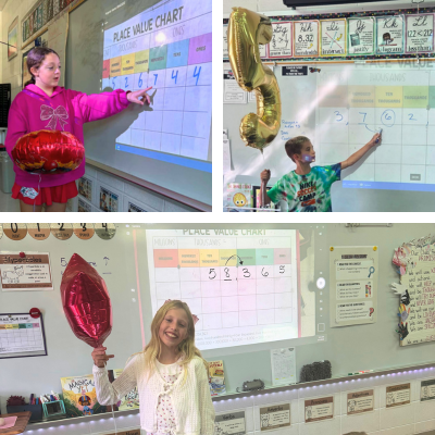 Fourth graders holding balloons while pointing to numbers on smart board.
