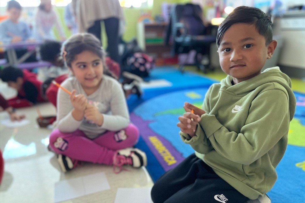 Two young students sitting on a mat while working in partner groups
