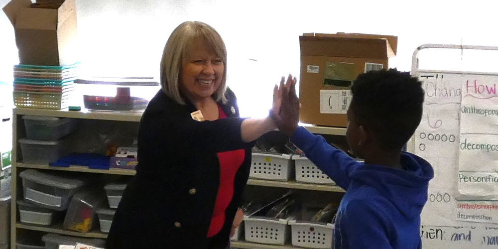 Organizers and donors stand arm in arm behind a mountain of backpacks stuffed with school supplies