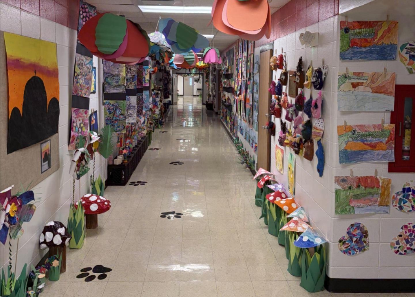 A hallway in a school. A variety of art projects made in a variety of media hung from the ceiling or hung on the wall.  