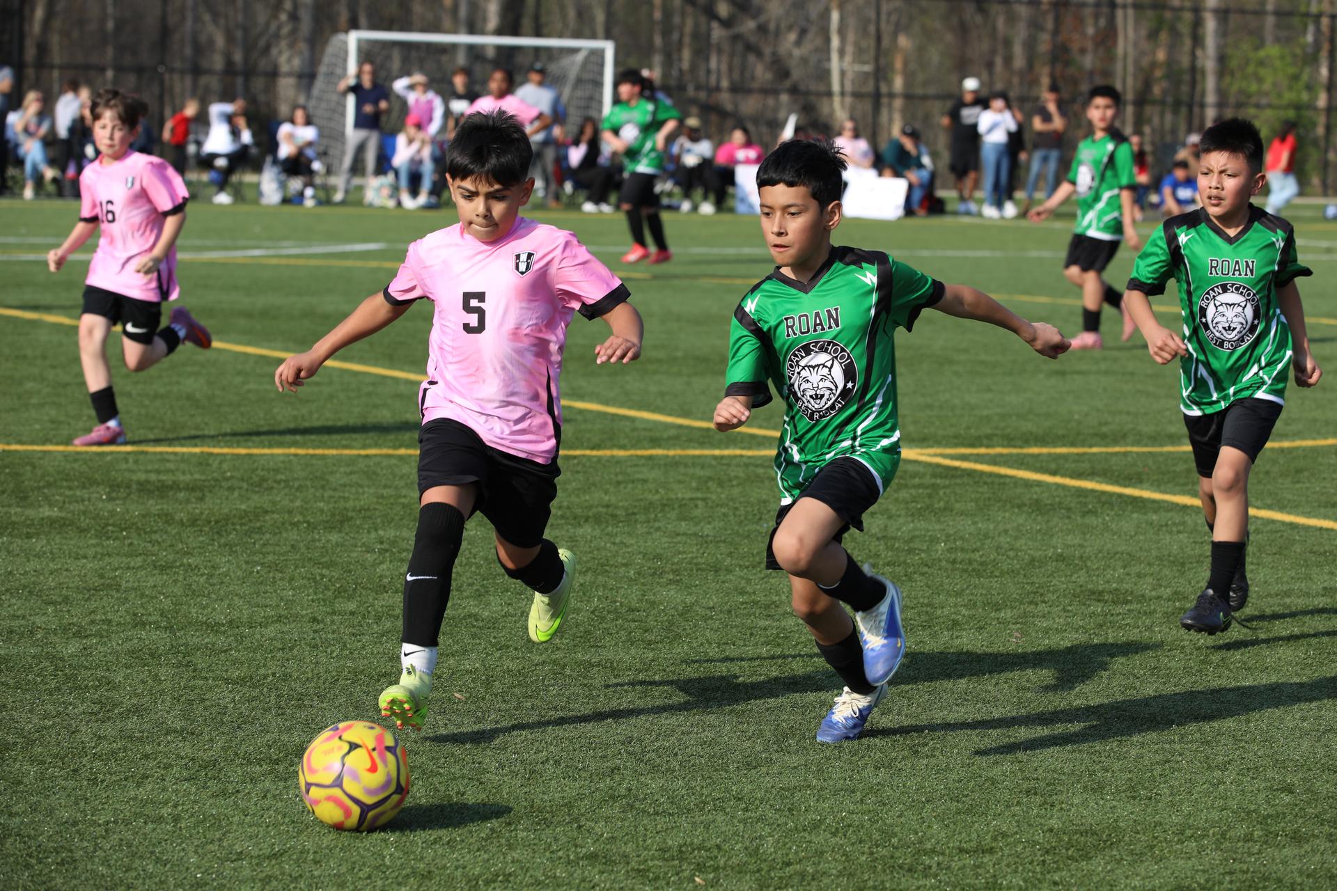 Students in pink and green soccer uniforms pass the soccer ball.