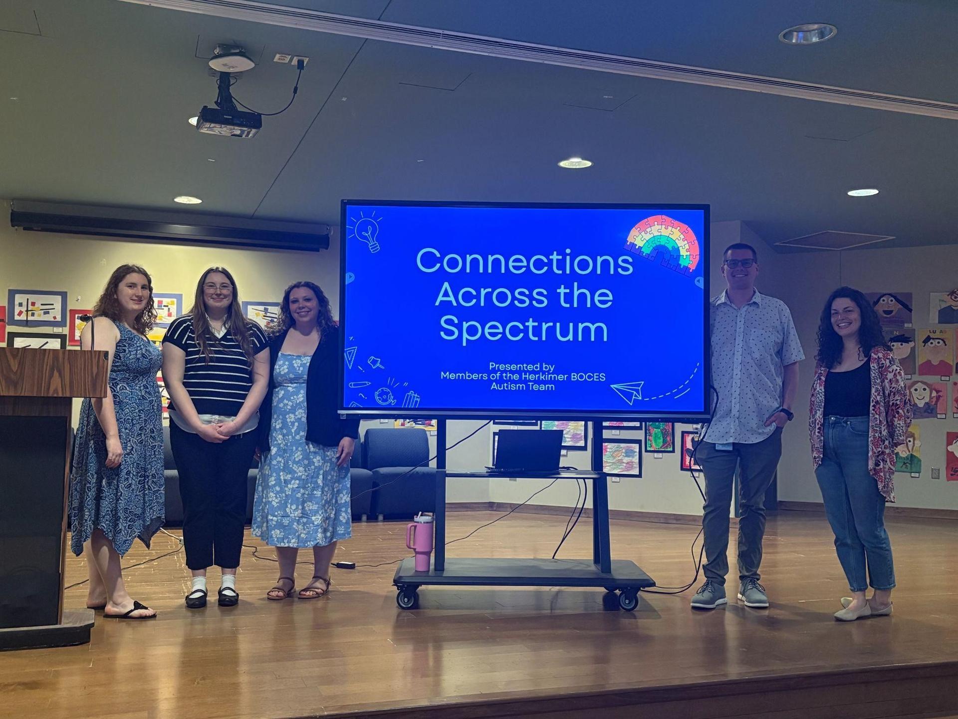 Several people standing on stage by a screen during Connections Across the Spectrum event