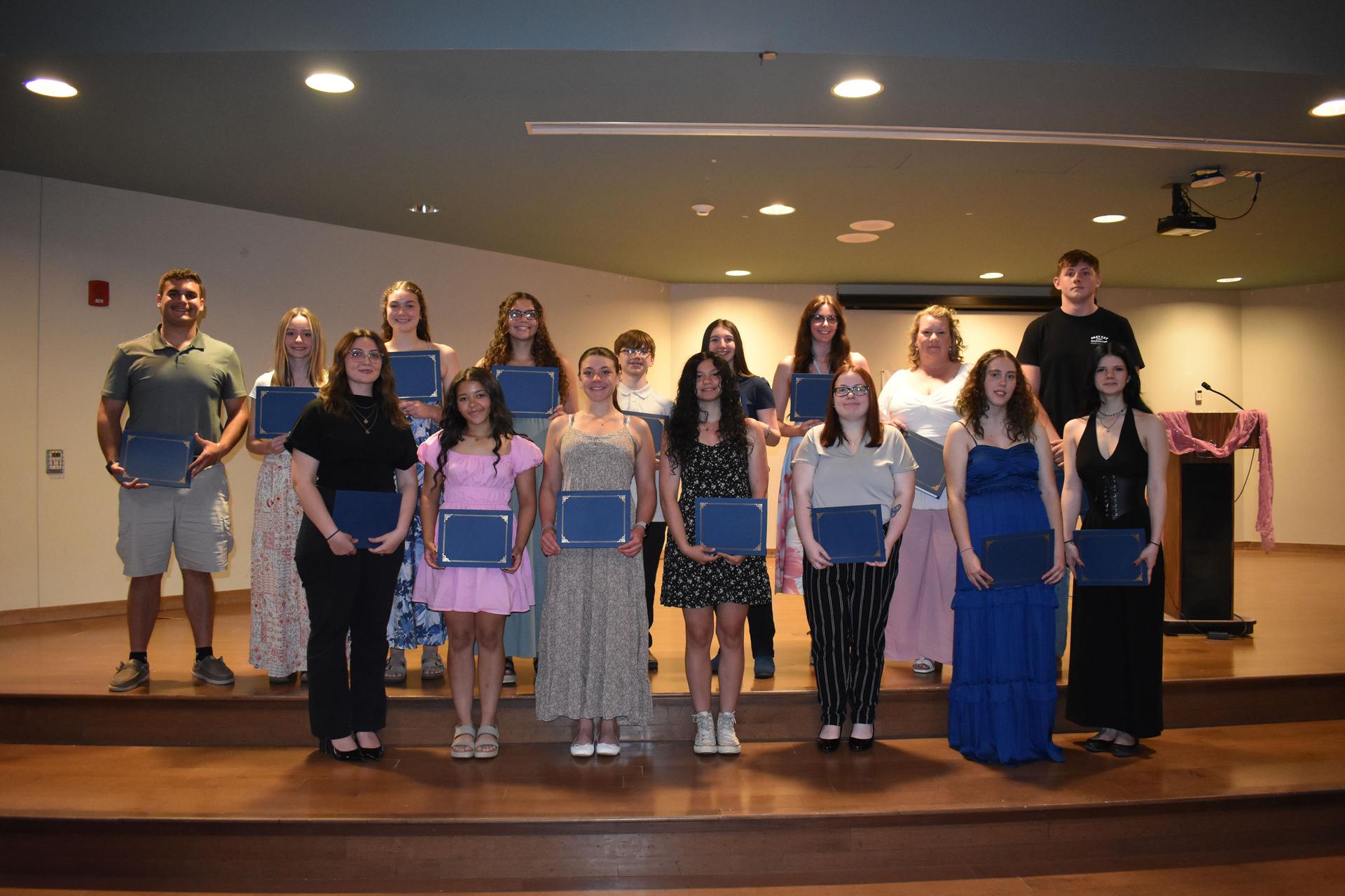Many students on stage posing with scholarship award certificates
