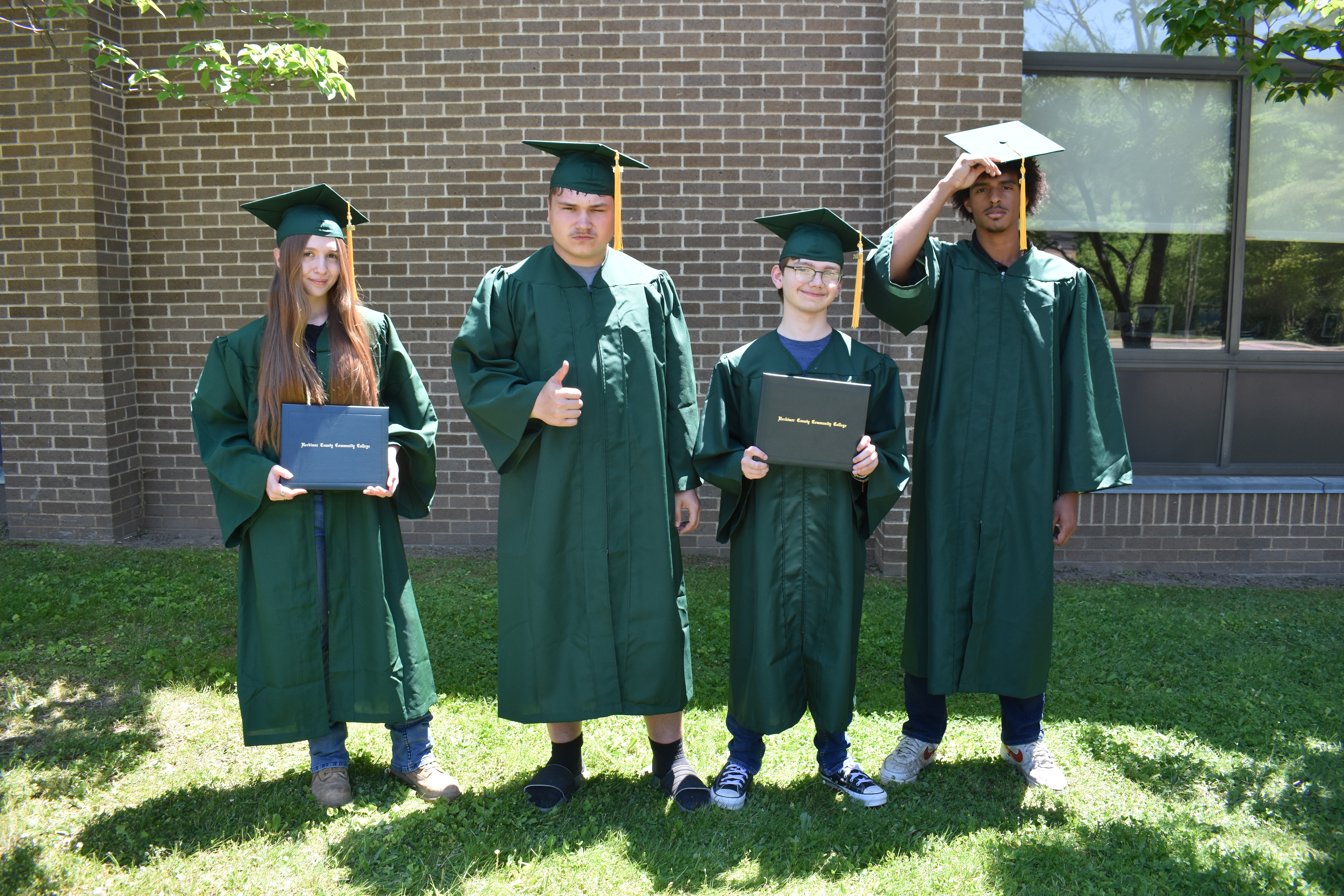 Four students posing outside in Herkimer College graduation caps and gowns