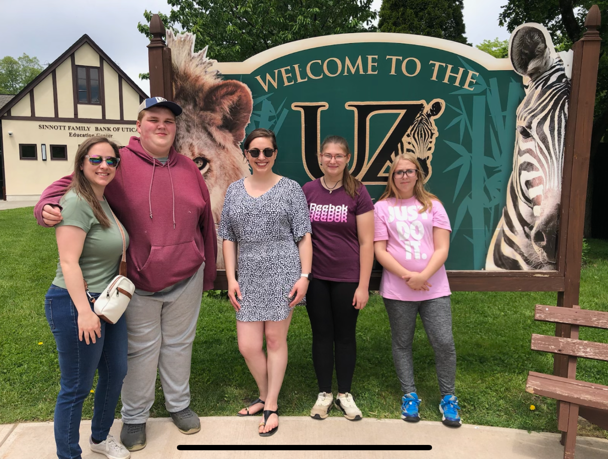 Several people posing by Utica Zoo sign at the zoo