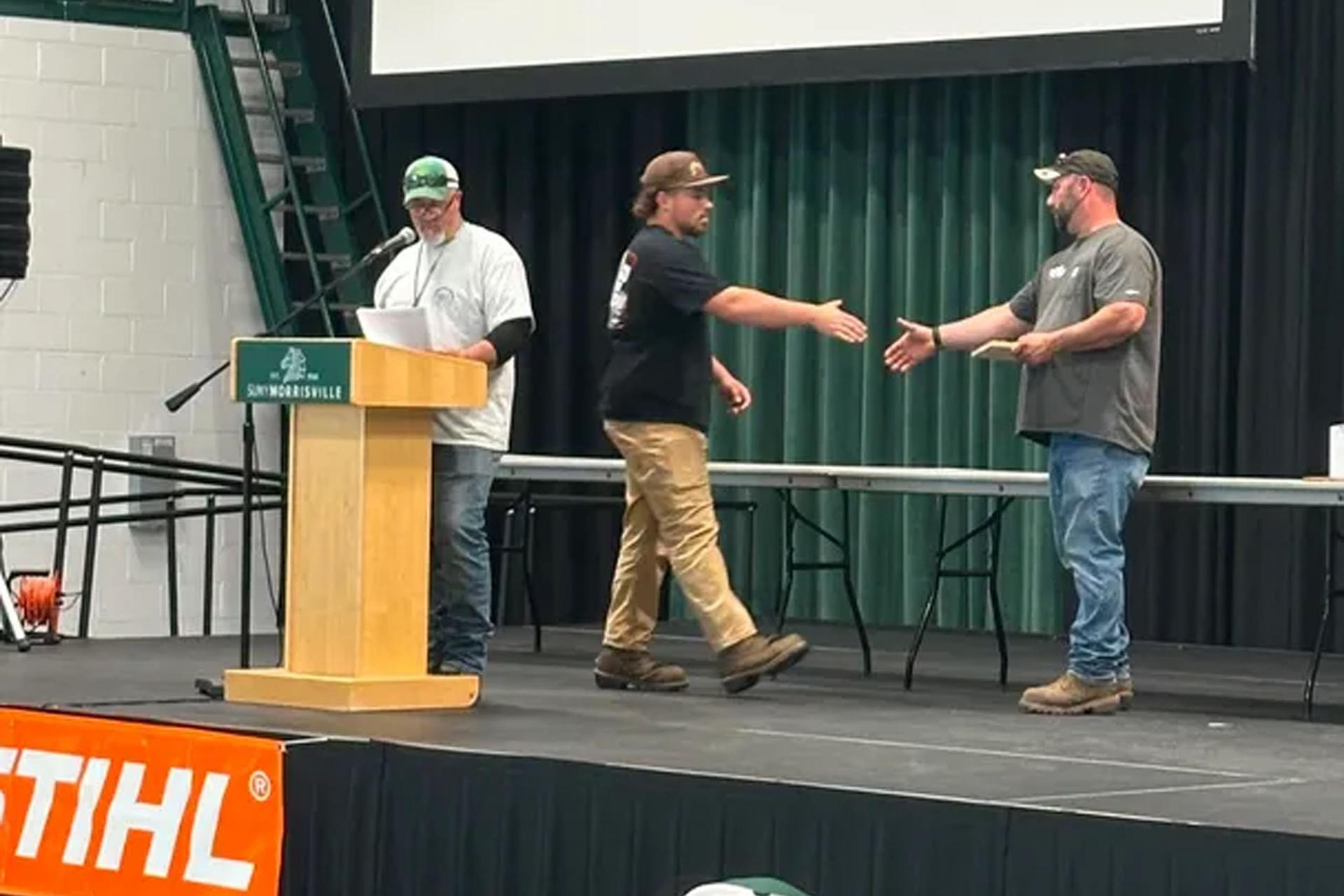 Student shaking hands on stage with another person speaking at podium