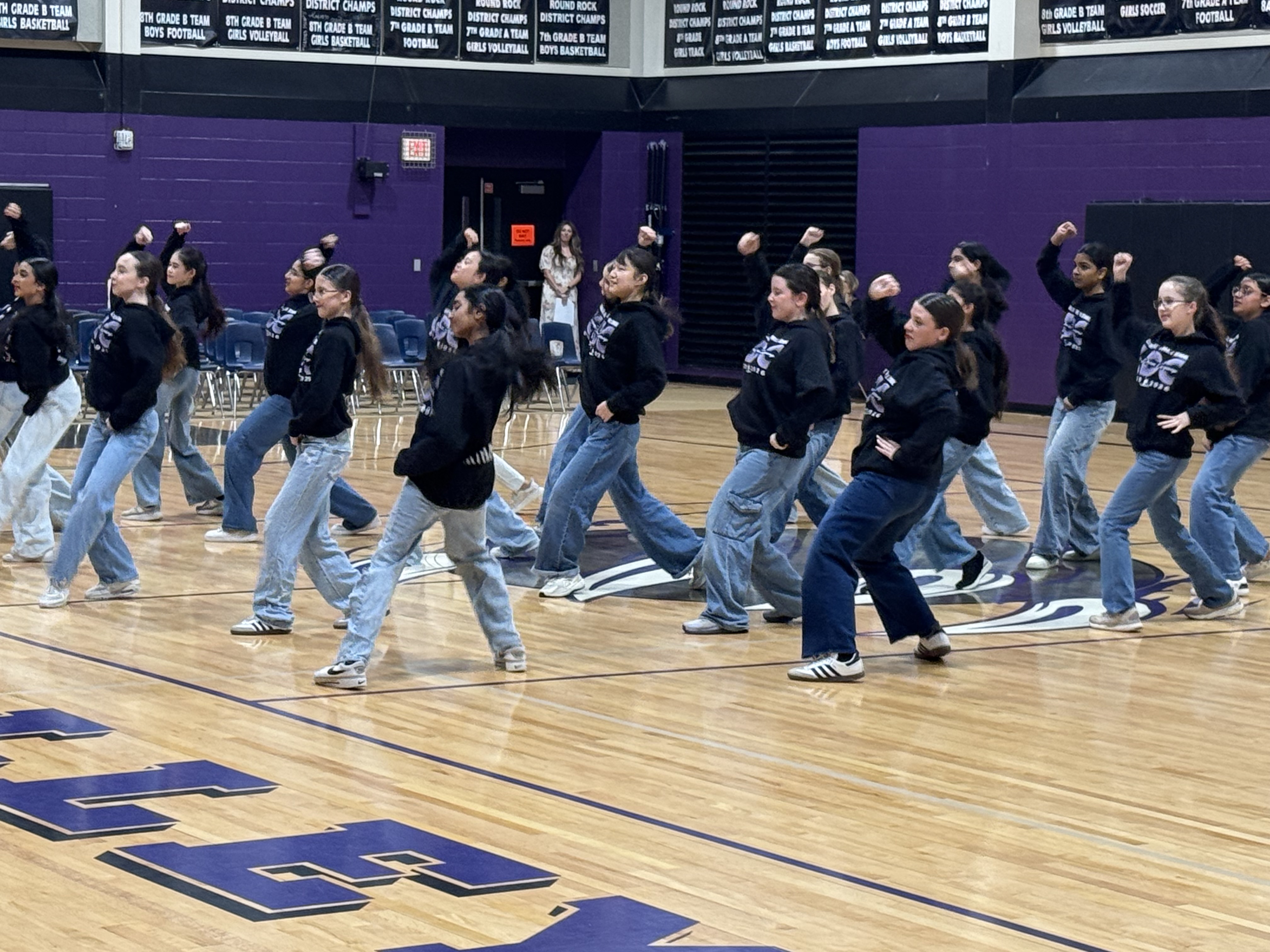 A group of middle school students performing a synchronized dance routine on a gymnasium basketball court.