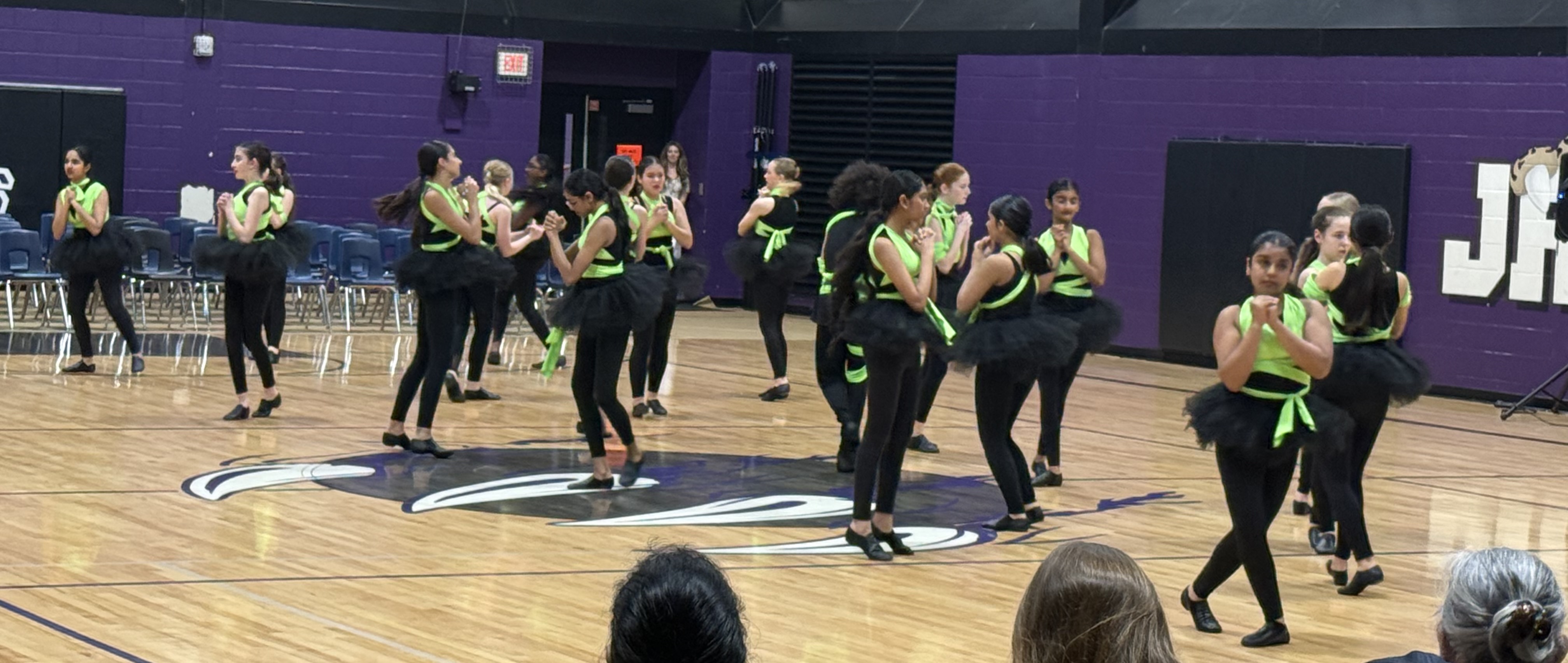 A group of middle school students performing a synchronized dance routine on a gymnasium basketball court.