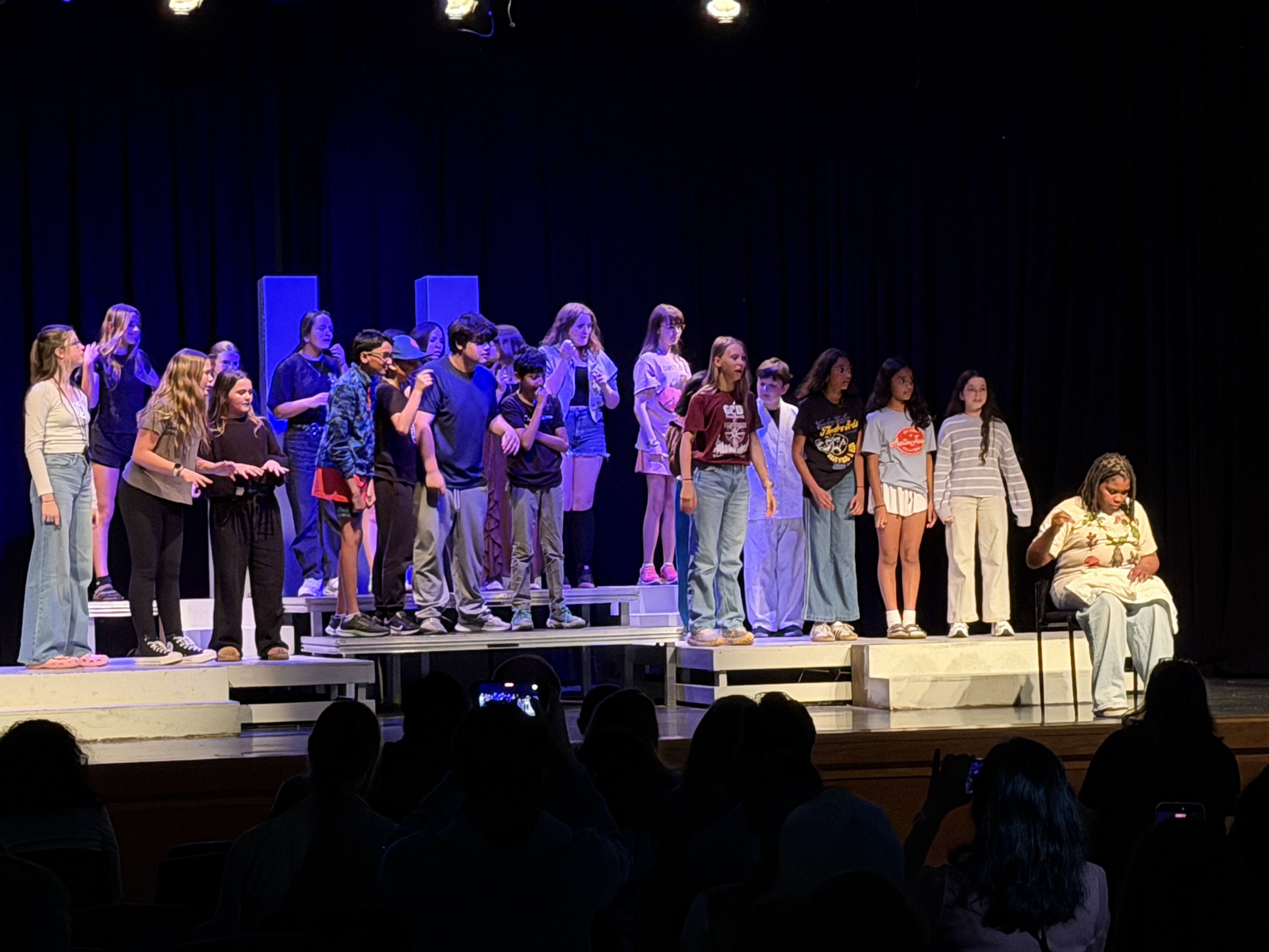 A wide shot from the audience's perspective of a large group of middle school students performing on a stage.