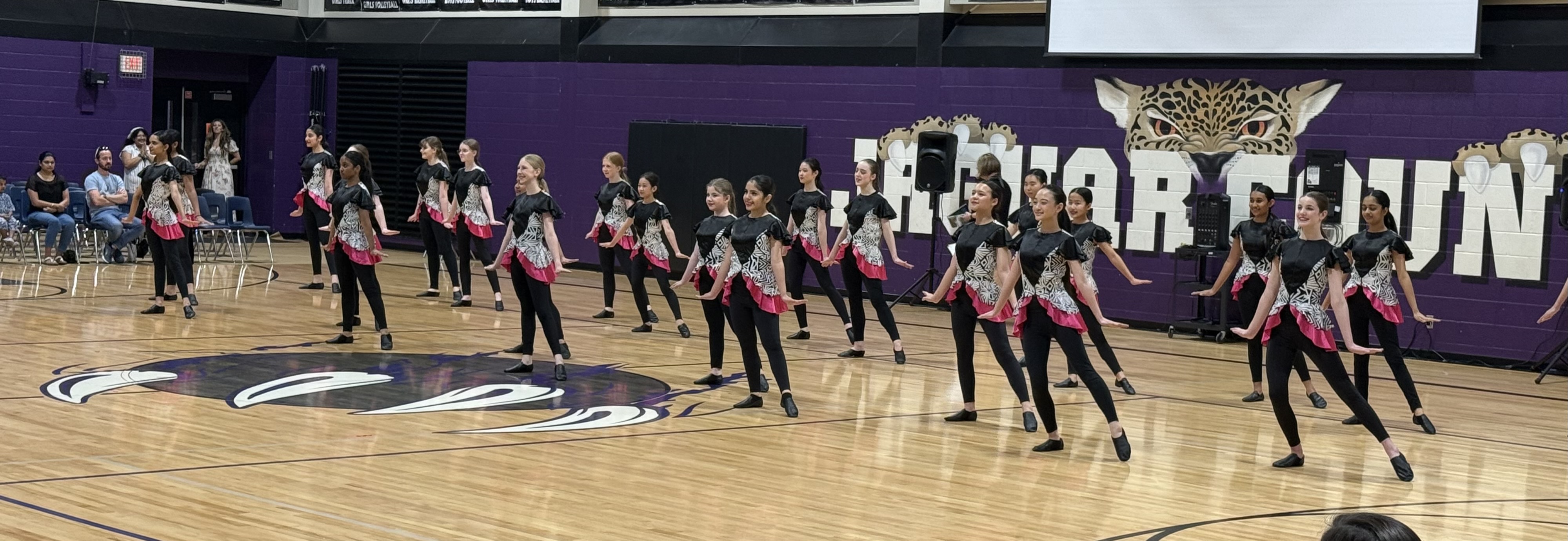 A group of middle school students performing a synchronized dance routine on a gymnasium basketball court.