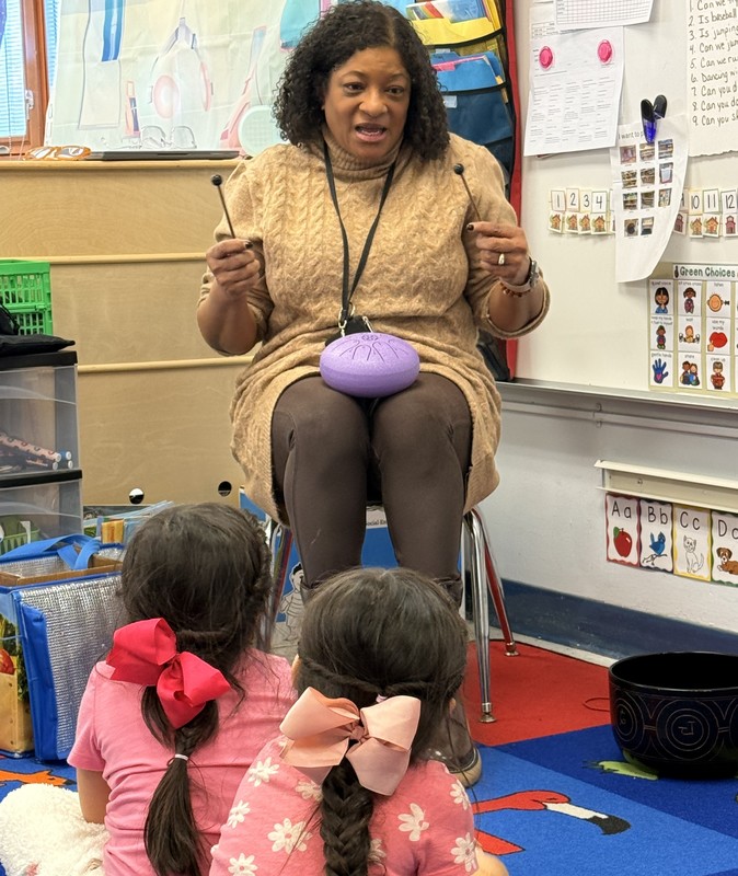Principal Torres sitting and holding a chime while students sit on the floor and listen to her talk