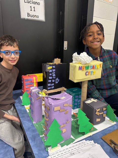 Two students show off their urban model called New Paint City, made from cardboard and construction paper