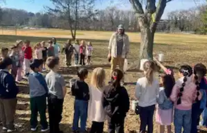 Aaron Stoler speaking under a large tree outdoors surrounded by a group of students