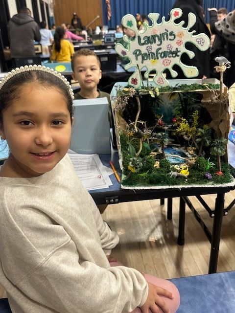 A student with her habitat model that has moss and sticks showing a rainforest