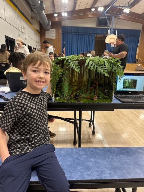 A student shows off his habitat model that has ferns and trees representing a forest
