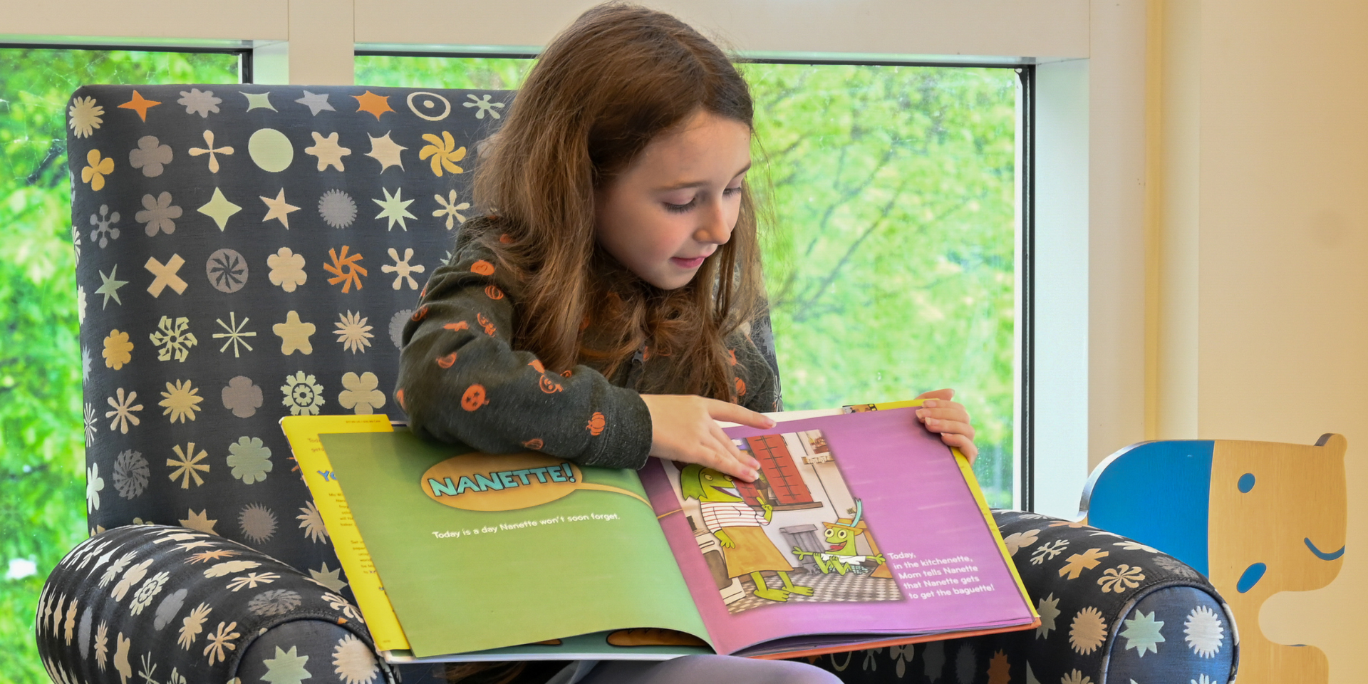 Student sitting in a chair reading a book to an audience