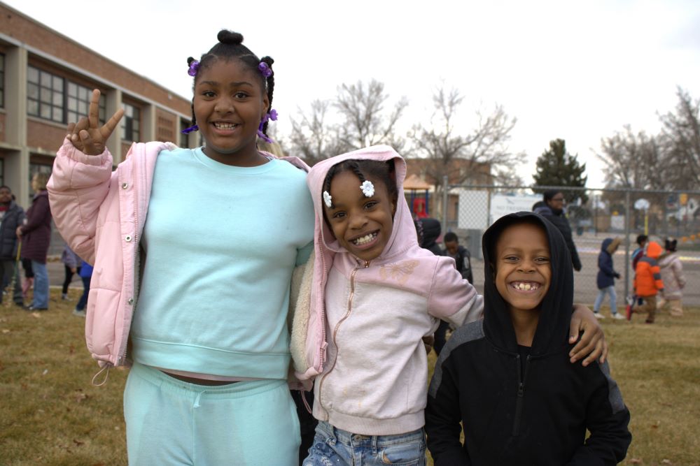 3 Hallett students smile at the camera and hold up peace signs