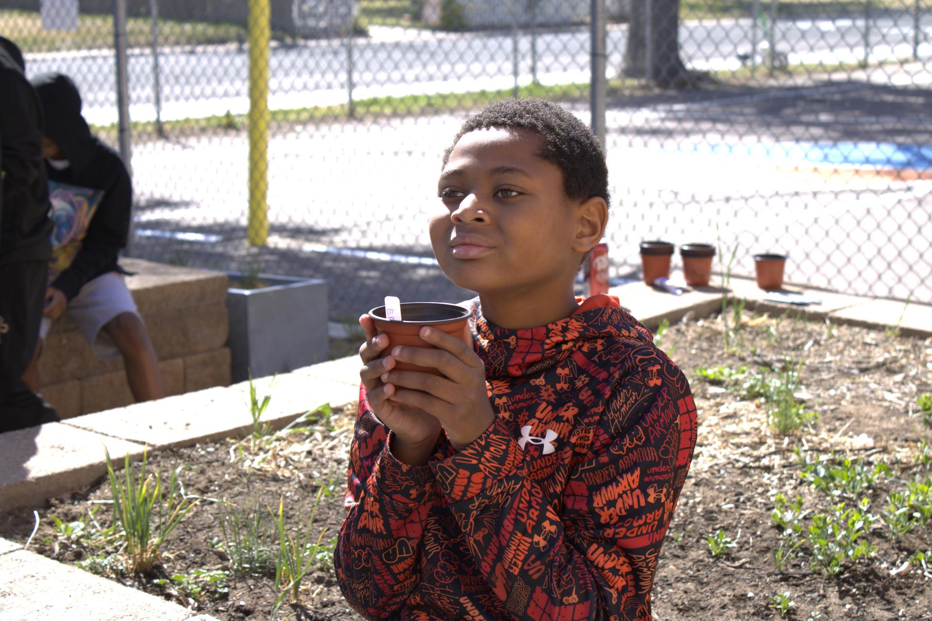 Hallett student holds a potted plant in the garden