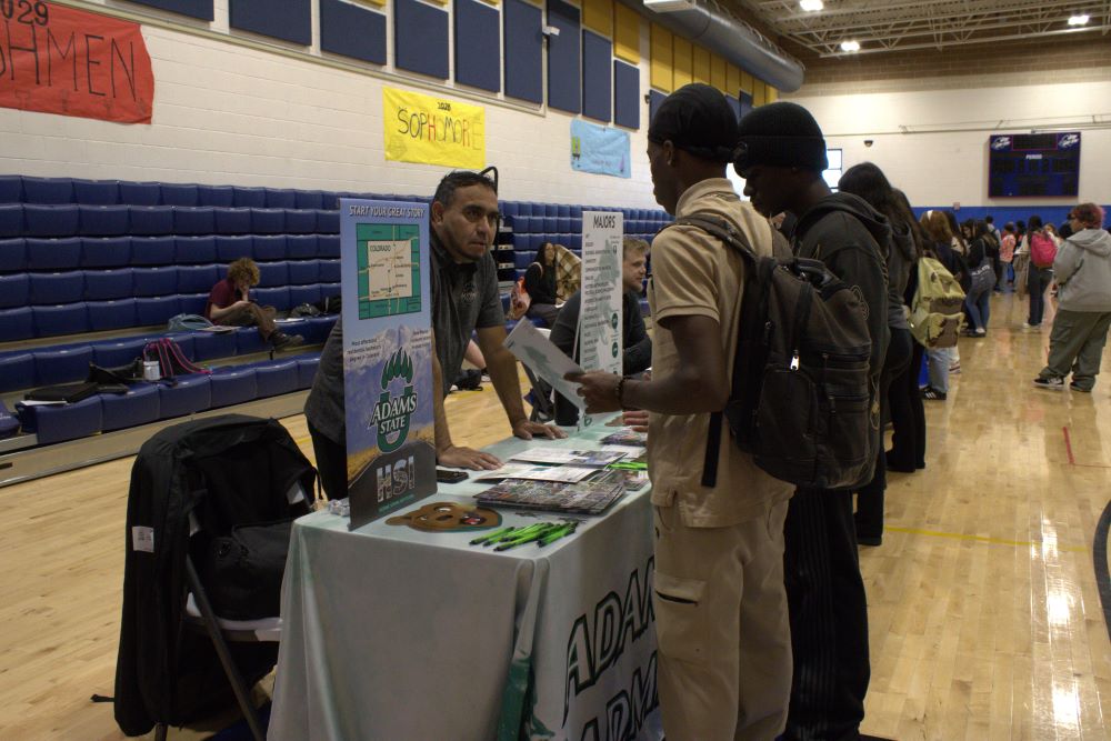 NEC students stand at a table in the gym during a college fair.