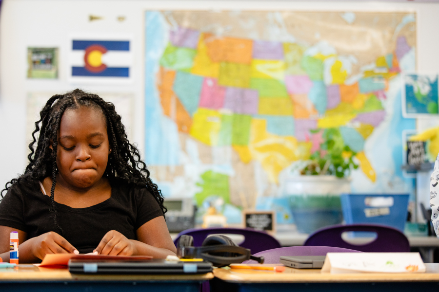 Hallett student focuses at her desk with a map in the background