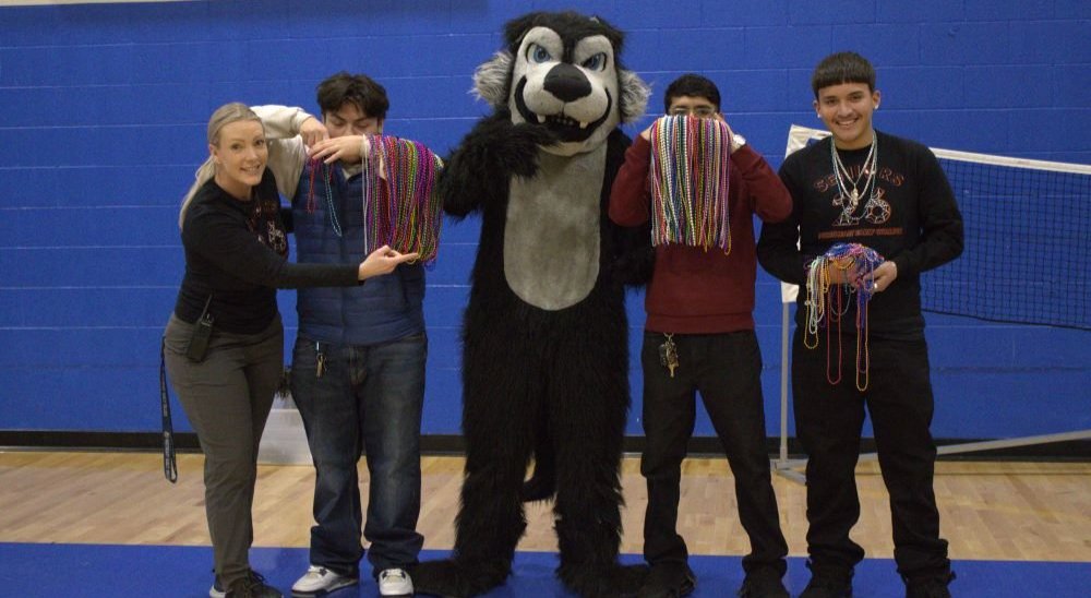 NEC Principal poses with Wolfie mascot, and 3 students holding up beads earned in a spirit week game
