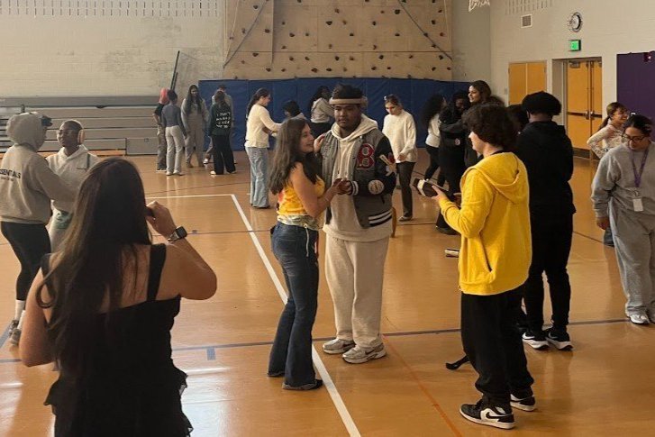 Students in a gymnasium learning how to salsa dance.