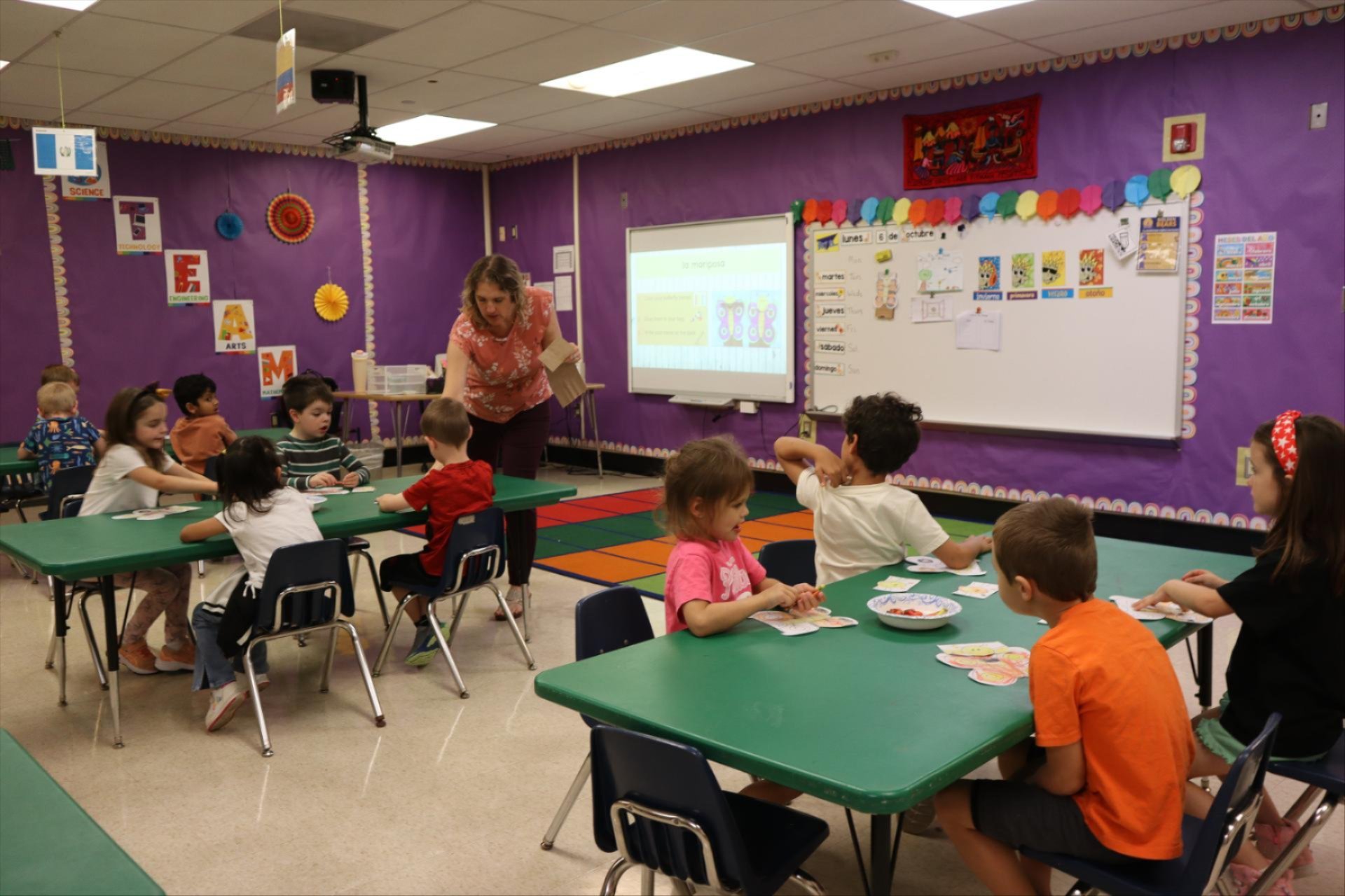 Children in a classroom engaged in activities with a teacher assisting.