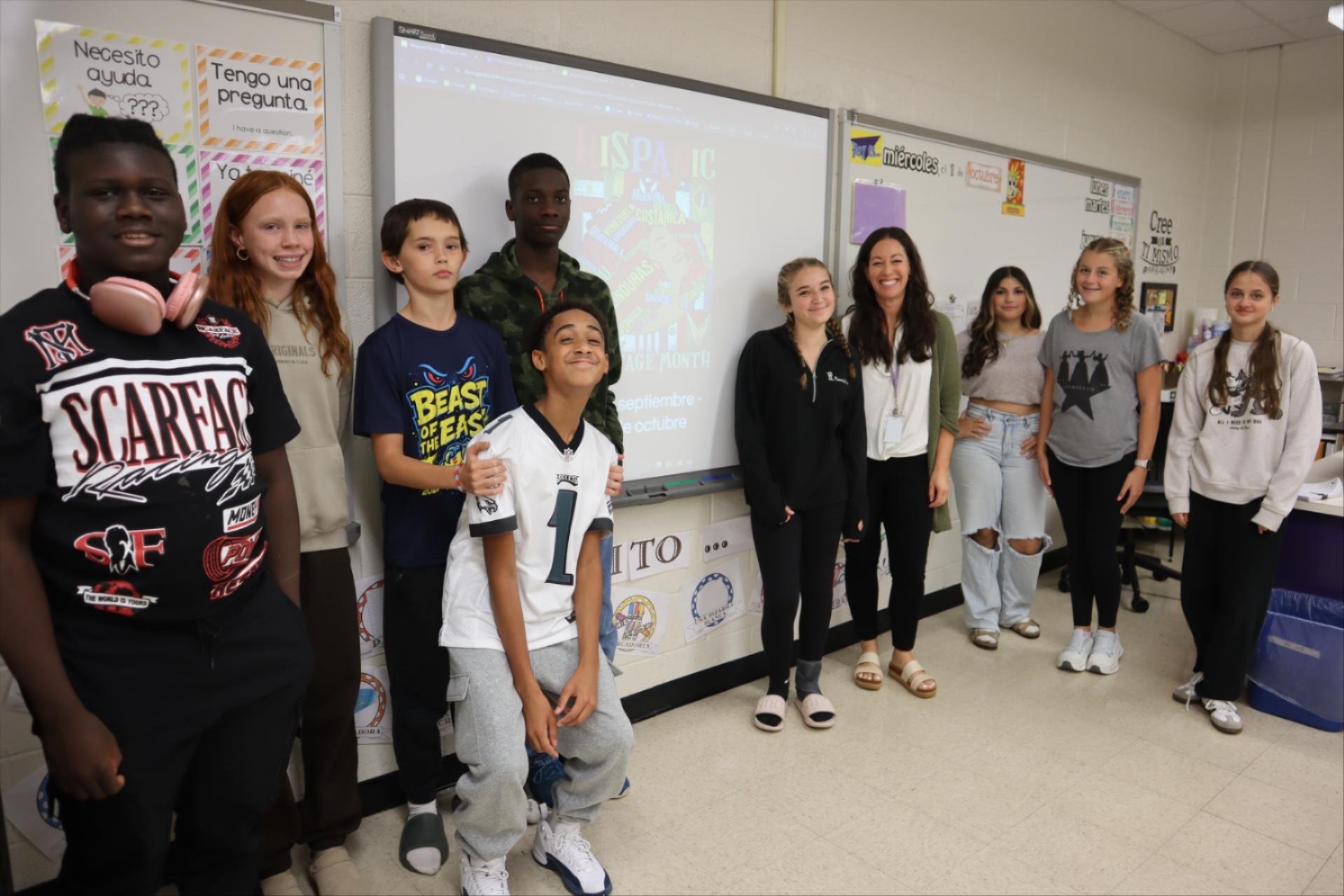 Group of students and their teacher standing in front of a projected image that says 