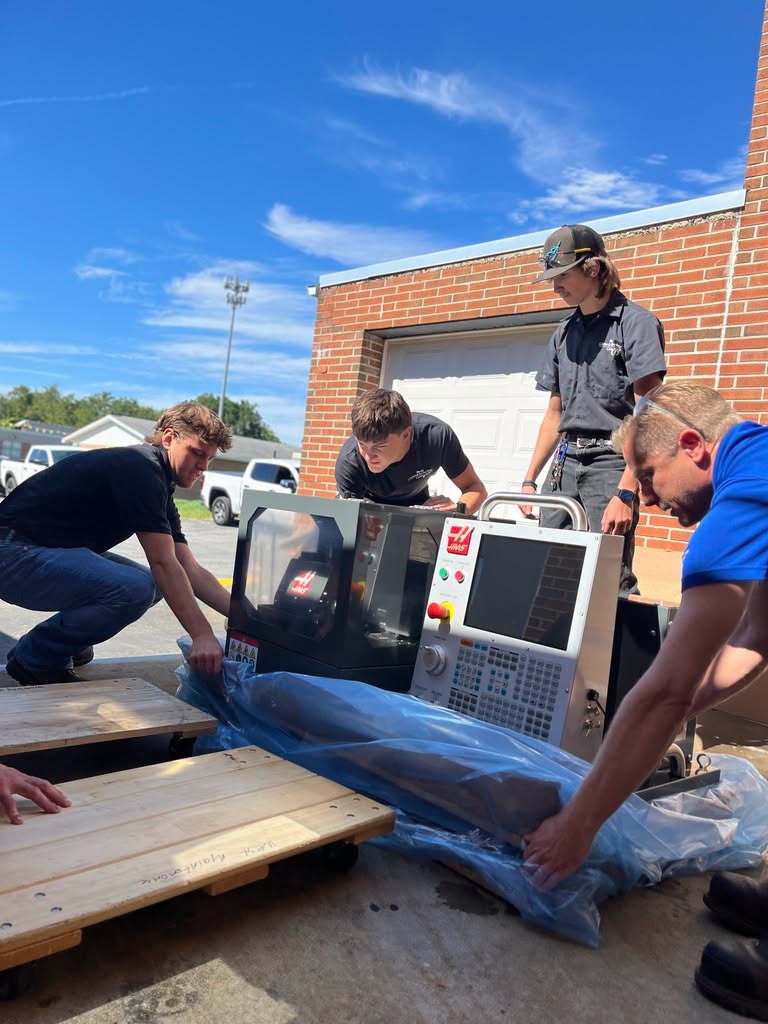 Three male students and one adult removing plastic from tabletop CNC machine