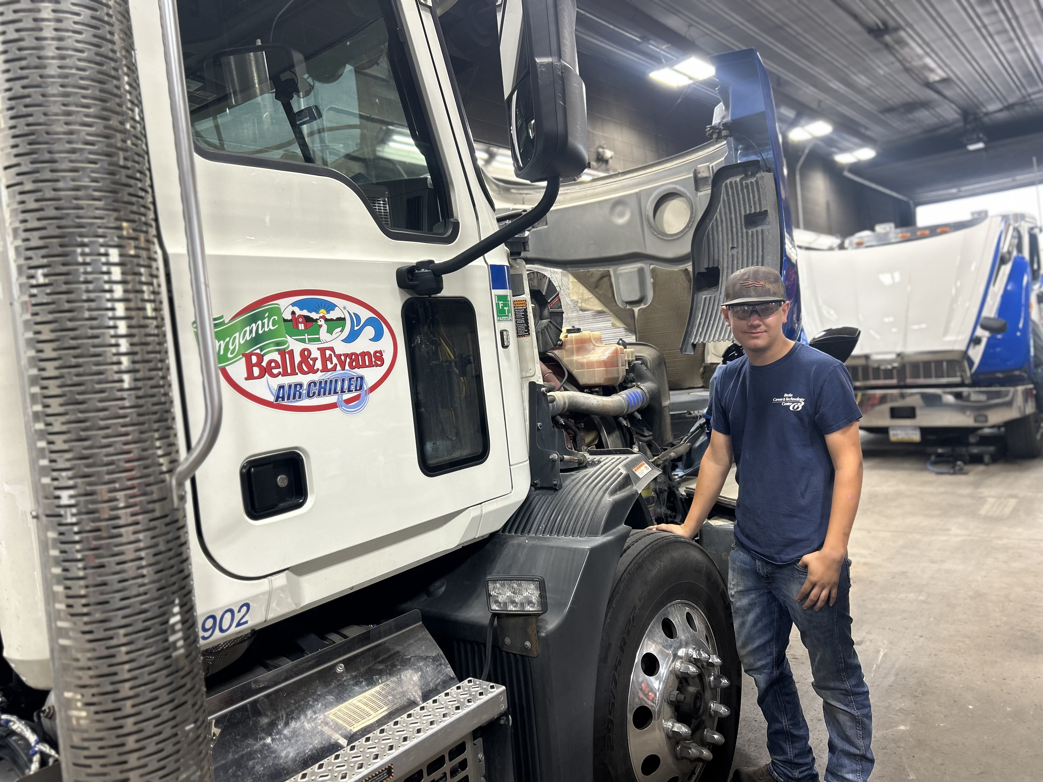 Male wearing a grey cap and navy shirt standing beside a Bell and Evans tractor trailer