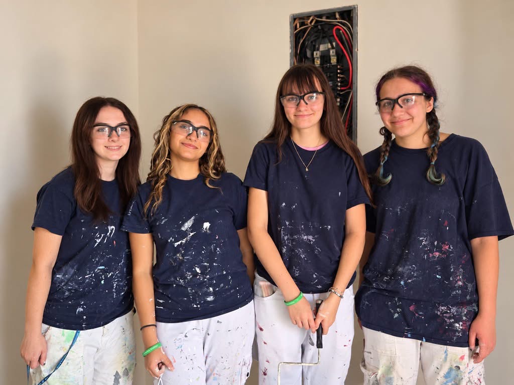 Four female students wearing safety glasses, navy shirts and white pants