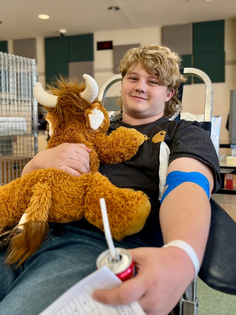 Male sitting in a lounge chair holding a stuffed animal and soda donating blood