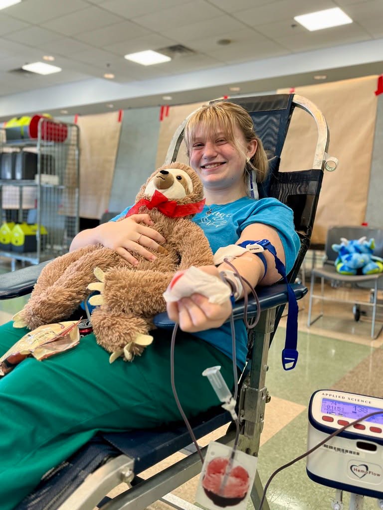 Female student sitting in a chair, holding a stuffed animal and donating blood