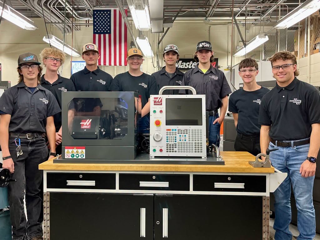 Eight male students wearing black shirts standing behind a desktop CNC maching