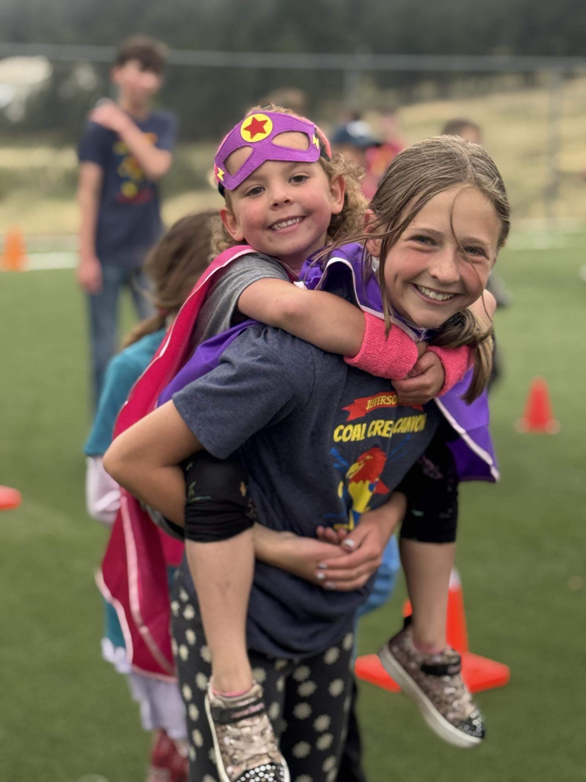 Image of a middle school aged girl with a kindergarten girl on her back, both are smiling. 