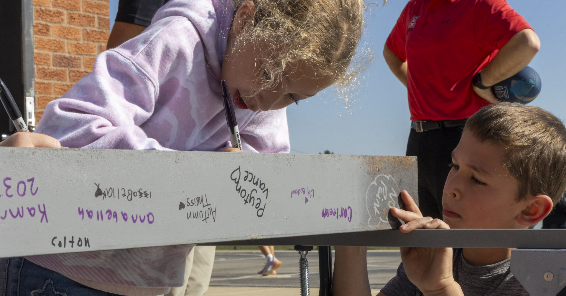 Two children, one girl and one boy, leaning over a table with a message board, looking at signatures.