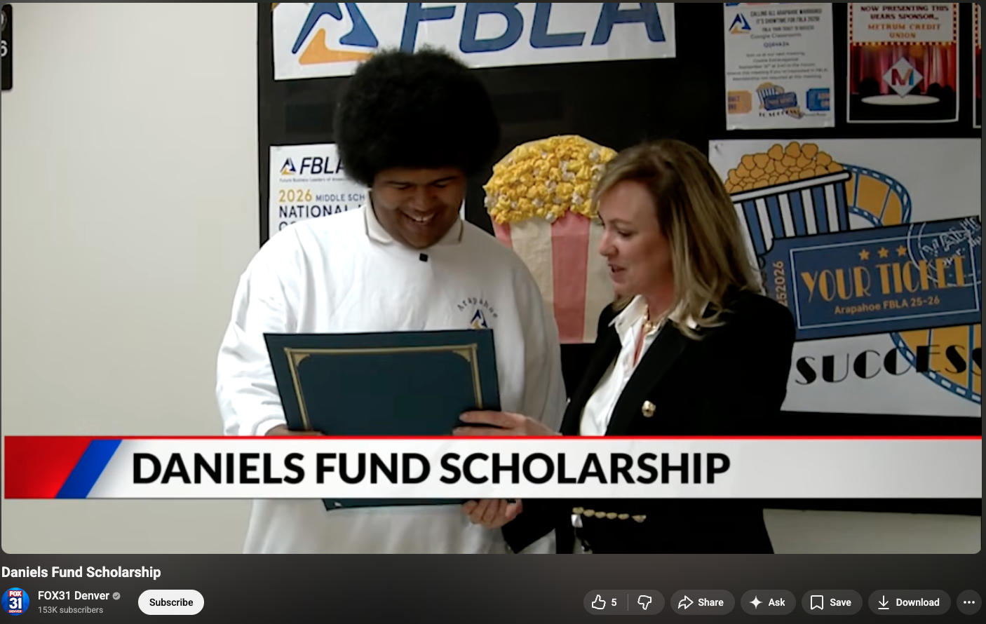 A student smiles as he receives a certificate from a woman; text reads 