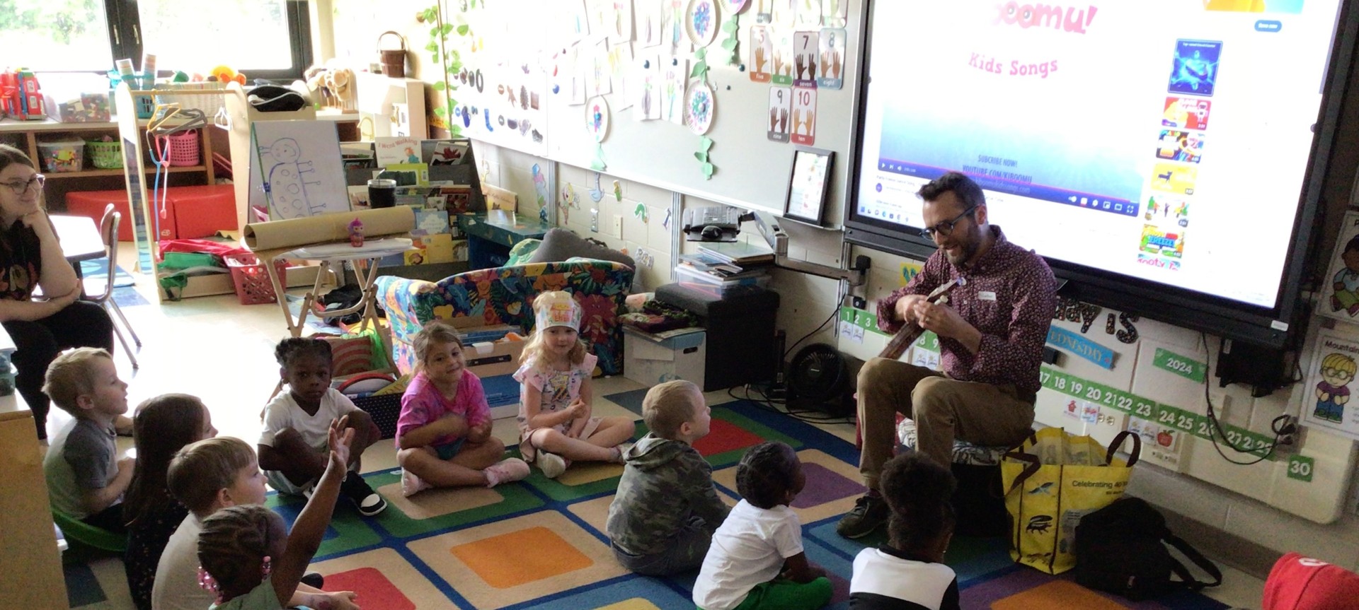 Teacher singing to students on carpet