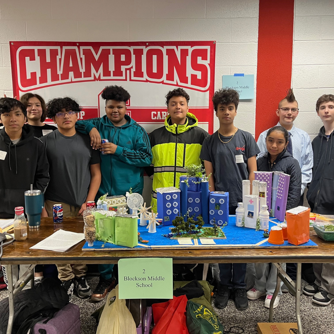 Students standing behind table with their city on the table in front of them